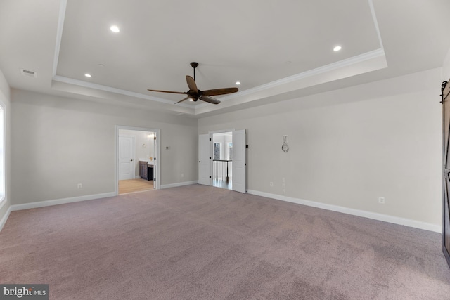 carpeted spare room featuring crown molding, a barn door, a tray ceiling, and ceiling fan