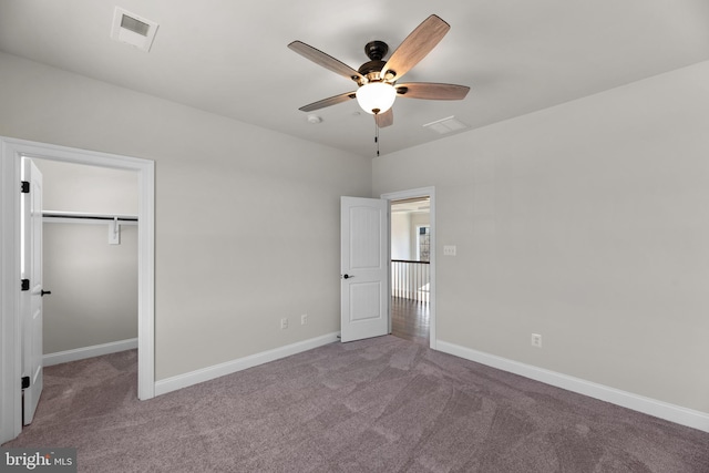 unfurnished bedroom featuring a spacious closet, light colored carpet, a closet, and ceiling fan