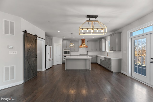 kitchen with white fridge with ice dispenser, a barn door, a center island, pendant lighting, and dark hardwood / wood-style floors