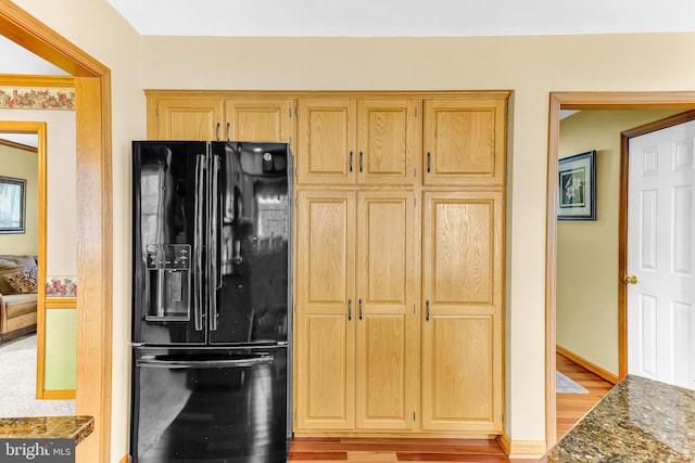 kitchen with light brown cabinetry, dark stone counters, light wood-type flooring, and black fridge