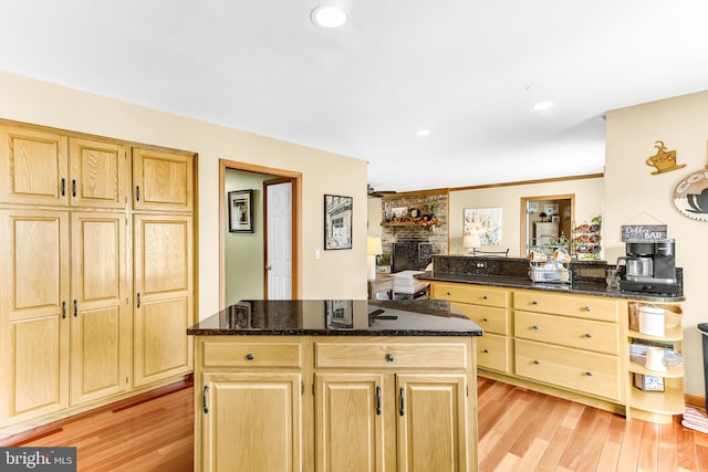 kitchen with a center island, a fireplace, light wood-type flooring, and dark stone countertops