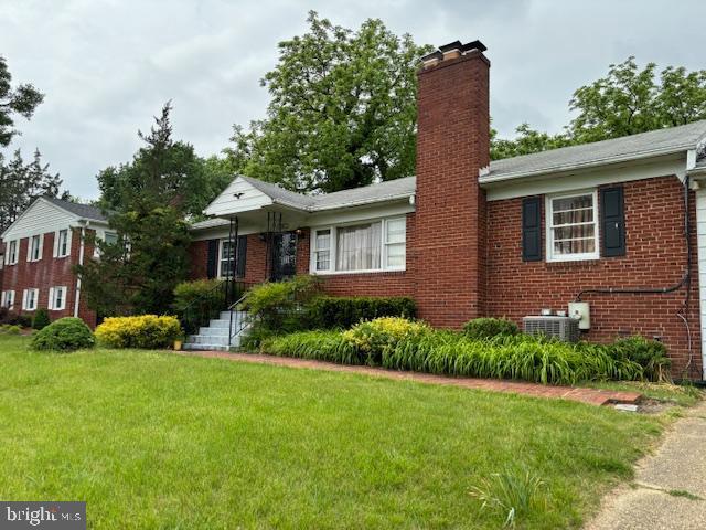 ranch-style house with a chimney, brick siding, a front lawn, and central AC unit