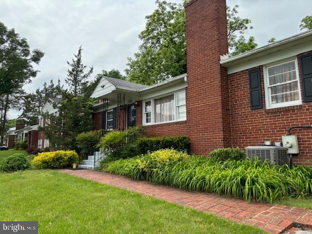 view of property exterior with a lawn, brick siding, a chimney, and central AC unit
