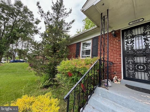 doorway to property featuring a yard and brick siding