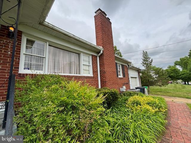 view of side of home featuring brick siding, an attached garage, and a chimney