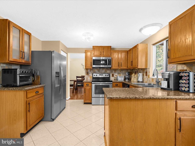 kitchen featuring kitchen peninsula, appliances with stainless steel finishes, backsplash, sink, and light tile patterned floors