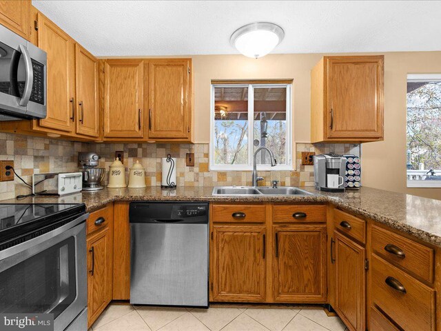 kitchen with backsplash, sink, dark stone countertops, light tile patterned floors, and stainless steel appliances