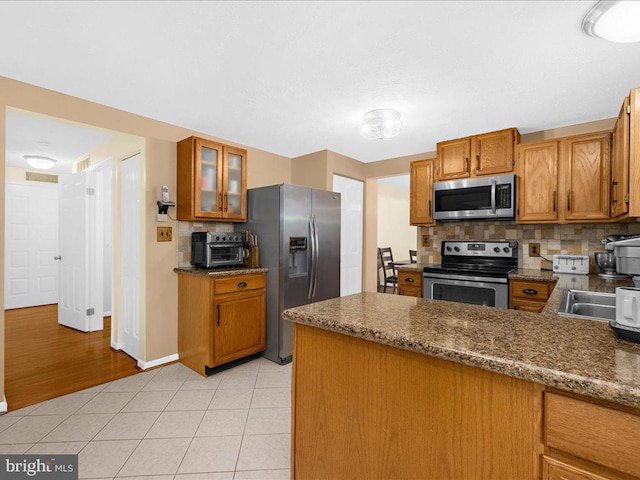 kitchen with light stone countertops, stainless steel appliances, kitchen peninsula, decorative backsplash, and light wood-type flooring