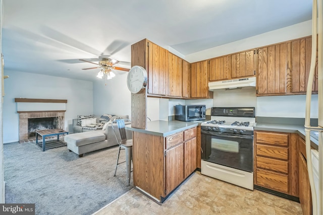 kitchen featuring a fireplace, kitchen peninsula, white range with gas stovetop, ceiling fan, and a breakfast bar