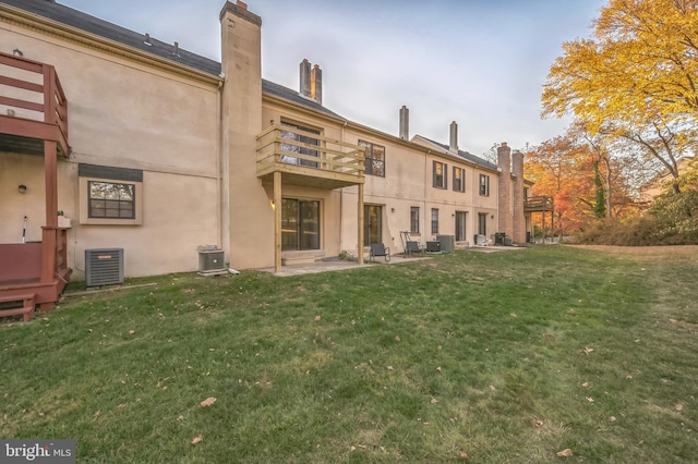 rear view of house with a balcony, central AC, a lawn, and a patio