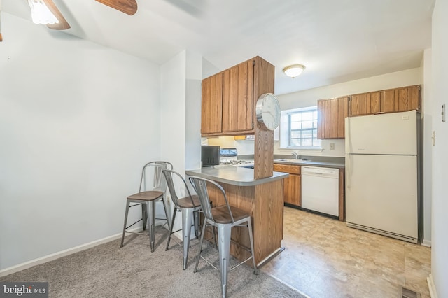 kitchen featuring kitchen peninsula, sink, a kitchen bar, white appliances, and ceiling fan