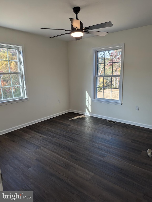 empty room with ceiling fan, a wealth of natural light, and dark hardwood / wood-style floors