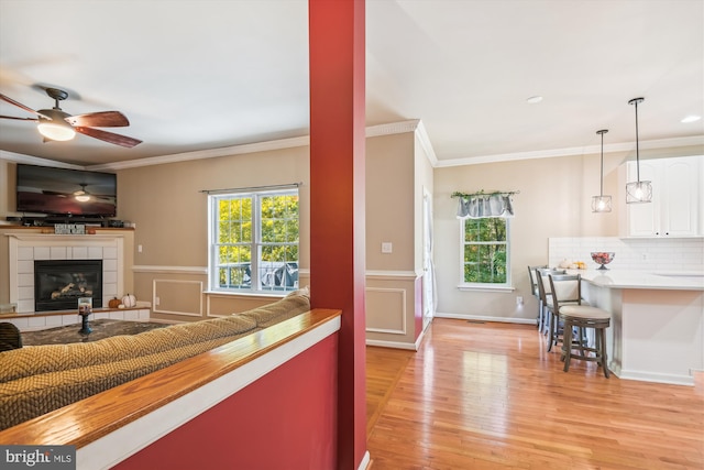 living room featuring crown molding, light hardwood / wood-style flooring, a fireplace, and ceiling fan