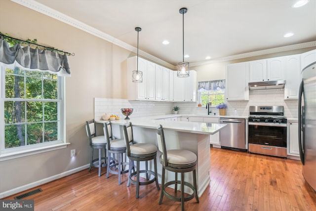 kitchen with kitchen peninsula, a breakfast bar, decorative light fixtures, white cabinetry, and appliances with stainless steel finishes