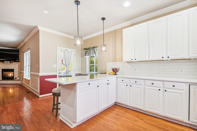 kitchen with white cabinets, kitchen peninsula, a tiled fireplace, and light hardwood / wood-style floors