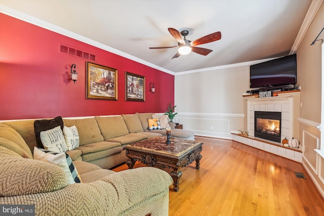 living room with ornamental molding, hardwood / wood-style flooring, a tiled fireplace, and ceiling fan