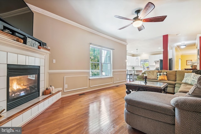 living room featuring ceiling fan, ornamental molding, a tile fireplace, and hardwood / wood-style floors