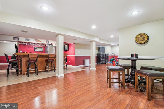 bar with light hardwood / wood-style floors and stainless steel fridge