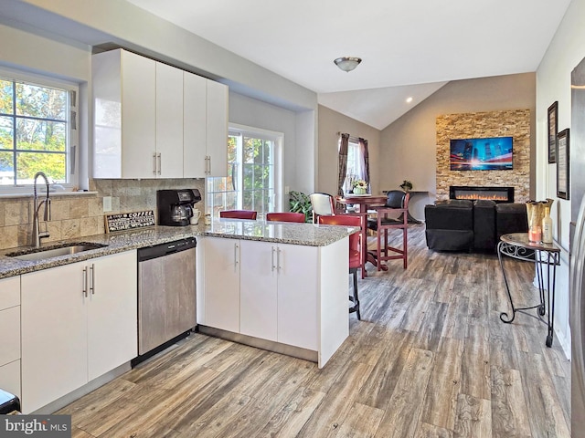 kitchen featuring kitchen peninsula, white cabinetry, stainless steel dishwasher, vaulted ceiling, and sink