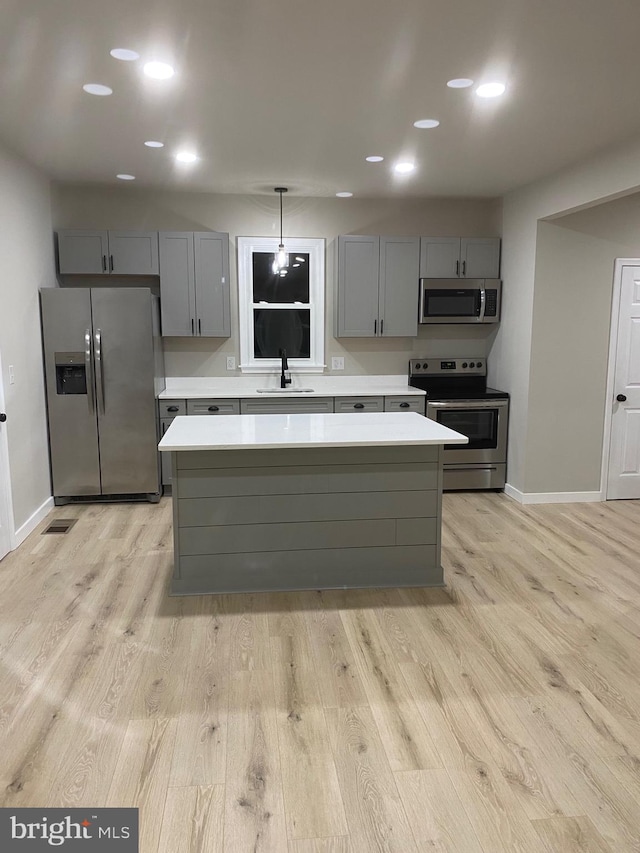 kitchen with gray cabinetry, light wood-type flooring, stainless steel appliances, and hanging light fixtures