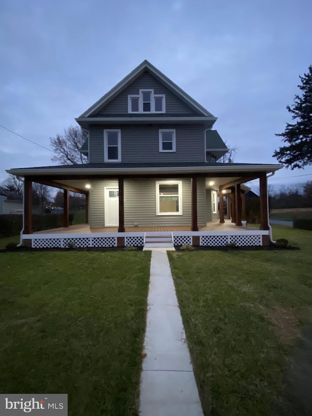 back house at dusk with a porch and a lawn