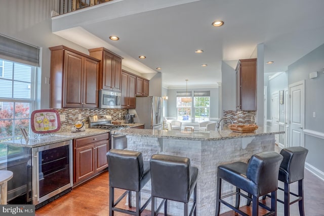 kitchen featuring appliances with stainless steel finishes, backsplash, hanging light fixtures, wine cooler, and light hardwood / wood-style flooring