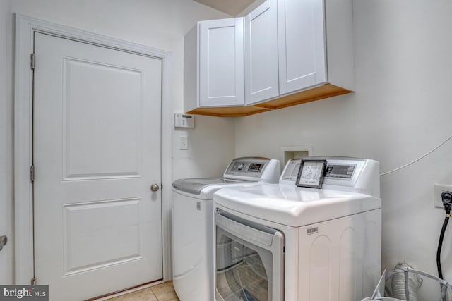 laundry area featuring washer and dryer, cabinets, and light tile patterned floors