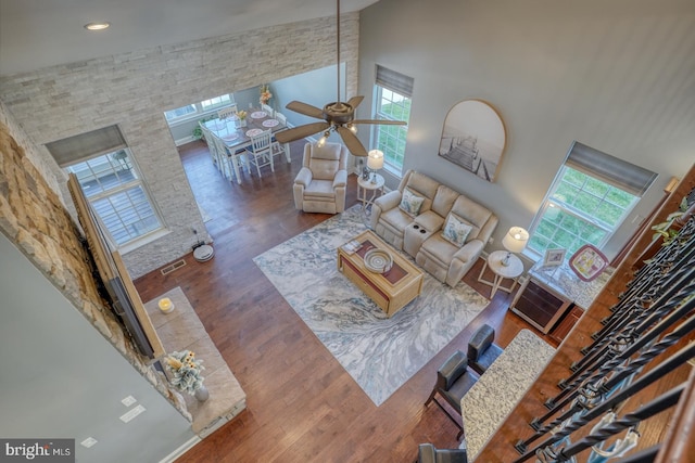 living room with a towering ceiling, ceiling fan, dark wood-type flooring, and a wealth of natural light