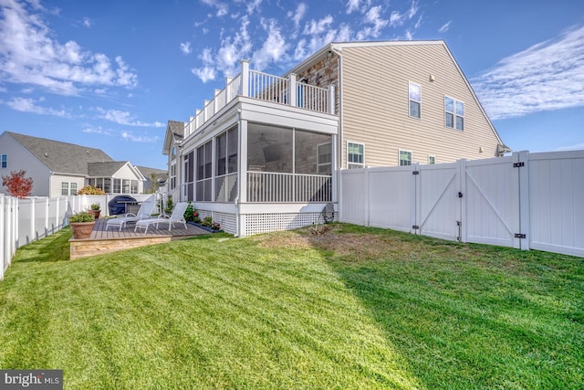 back of property with a wooden deck, a sunroom, and a lawn