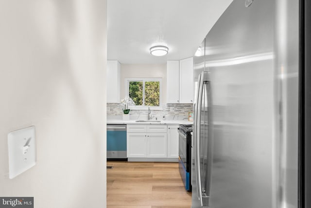 kitchen featuring white cabinetry, tasteful backsplash, a sink, appliances with stainless steel finishes, and light wood-type flooring