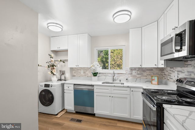 kitchen with washer / clothes dryer, white cabinetry, light hardwood / wood-style flooring, sink, and stainless steel appliances