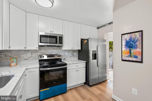 kitchen featuring decorative backsplash, white cabinets, light stone countertops, light hardwood / wood-style floors, and stainless steel appliances