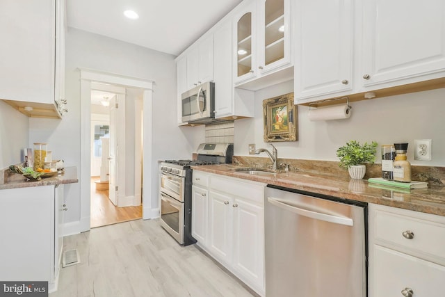 kitchen featuring appliances with stainless steel finishes, white cabinetry, stone countertops, light hardwood / wood-style floors, and sink