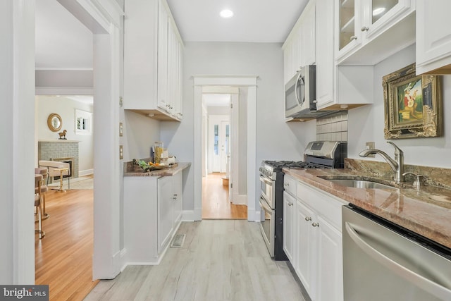 kitchen featuring light hardwood / wood-style flooring, sink, white cabinetry, stone counters, and appliances with stainless steel finishes