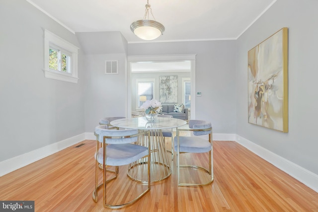 dining room with crown molding, light wood-type flooring, and a healthy amount of sunlight