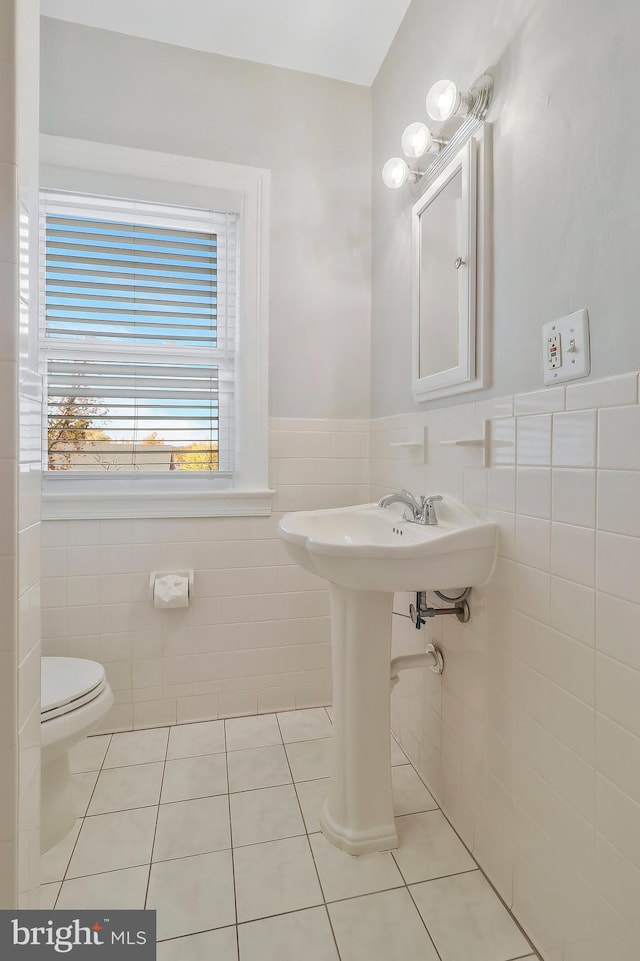 bathroom with toilet, tile patterned floors, and tile walls