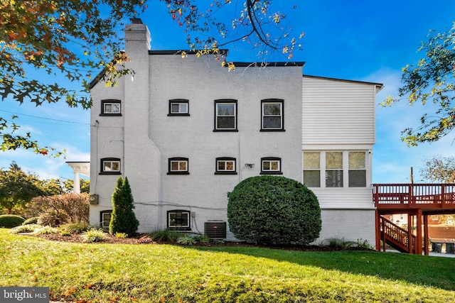 rear view of property featuring central AC, a wooden deck, and a lawn