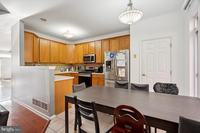 kitchen with tasteful backsplash, kitchen peninsula, decorative light fixtures, light tile patterned floors, and appliances with stainless steel finishes