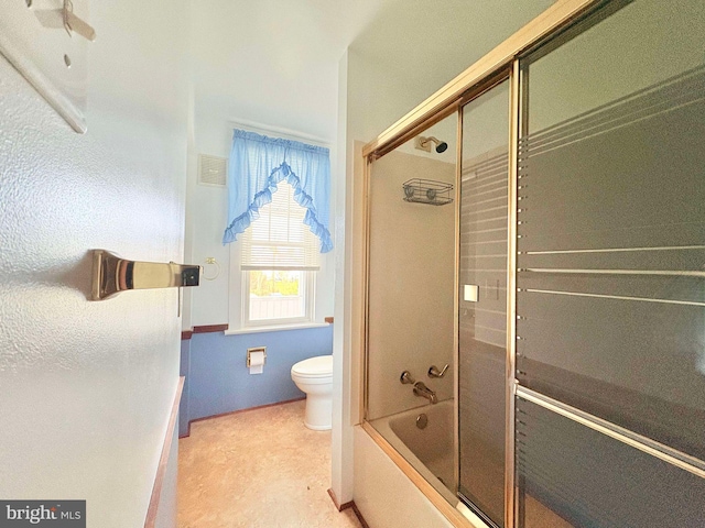 bathroom with toilet and bath / shower combo with glass door