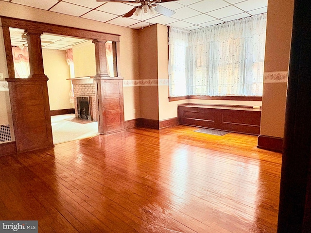 unfurnished room with a paneled ceiling, ceiling fan, light hardwood / wood-style floors, and a brick fireplace