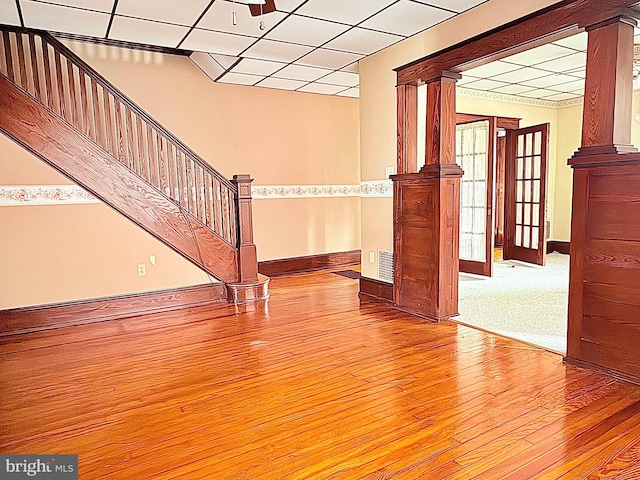 unfurnished living room featuring ornate columns, a drop ceiling, and wood-type flooring