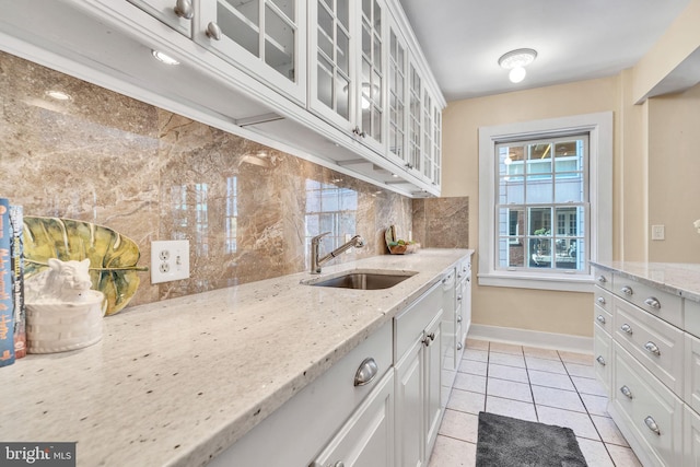 kitchen featuring backsplash, sink, light stone countertops, light tile patterned floors, and white cabinets