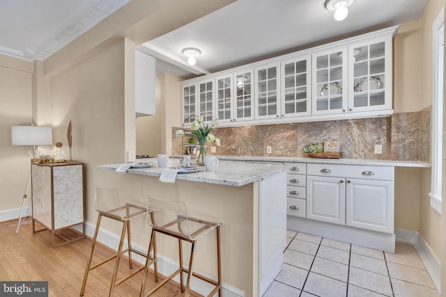 kitchen with a kitchen bar, light wood-type flooring, kitchen peninsula, white cabinets, and light stone counters