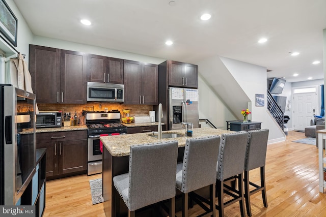 kitchen with light stone countertops, appliances with stainless steel finishes, a kitchen breakfast bar, light hardwood / wood-style flooring, and a center island with sink