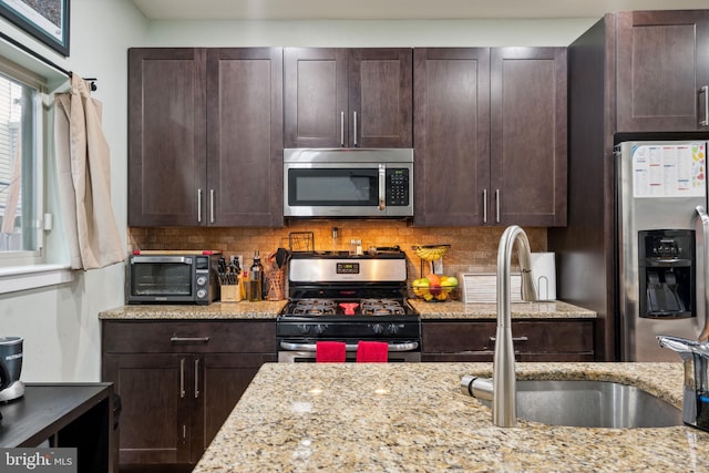 kitchen with light stone countertops, dark brown cabinetry, stainless steel appliances, and backsplash