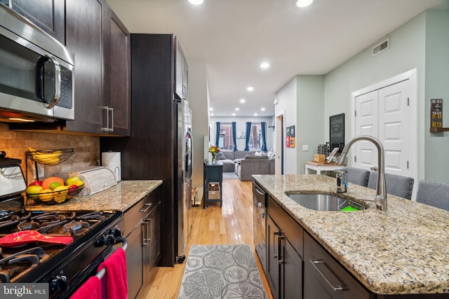 kitchen with decorative backsplash, an island with sink, stainless steel appliances, light stone countertops, and light hardwood / wood-style floors