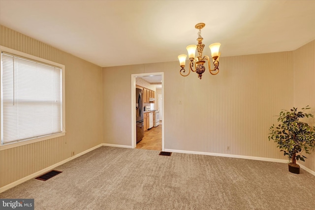 spare room featuring light carpet and an inviting chandelier