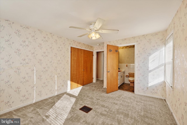 unfurnished bedroom featuring light carpet, connected bathroom, a closet, and ceiling fan