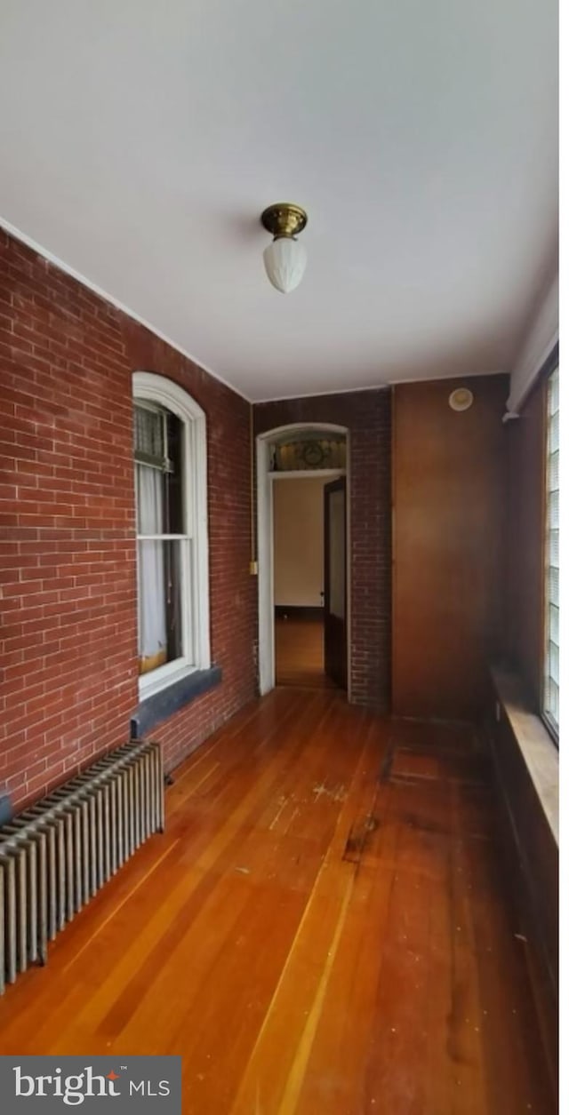 hallway with radiator heating unit, hardwood / wood-style floors, and brick wall