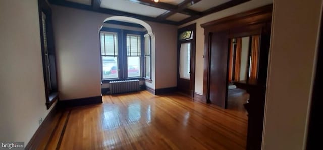 empty room featuring beamed ceiling, coffered ceiling, radiator heating unit, and light hardwood / wood-style flooring